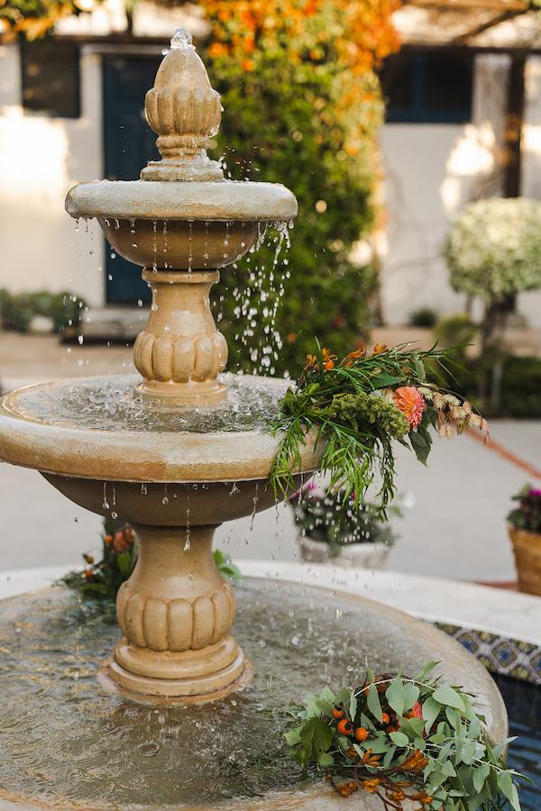 A beautiful courtyard fountain surrounded by vibrant flowers, with water gently flowing and creating a serene atmosphere.